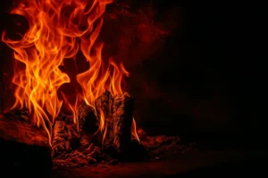 Bright flames engulfing burnt wood inside a darkened space, illustrating intense heat damage and the need for professional smoke removal and structural cleaning services.