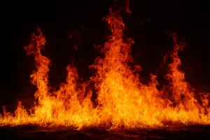 Bright orange flames surge upward in the dark, representing the destructive force of a building fire and the urgent need for cleanup and structural recovery efforts.